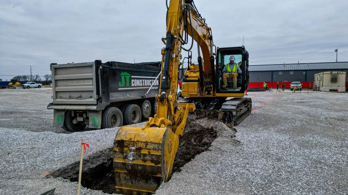 Excavator digging beside JT Construction dump truck